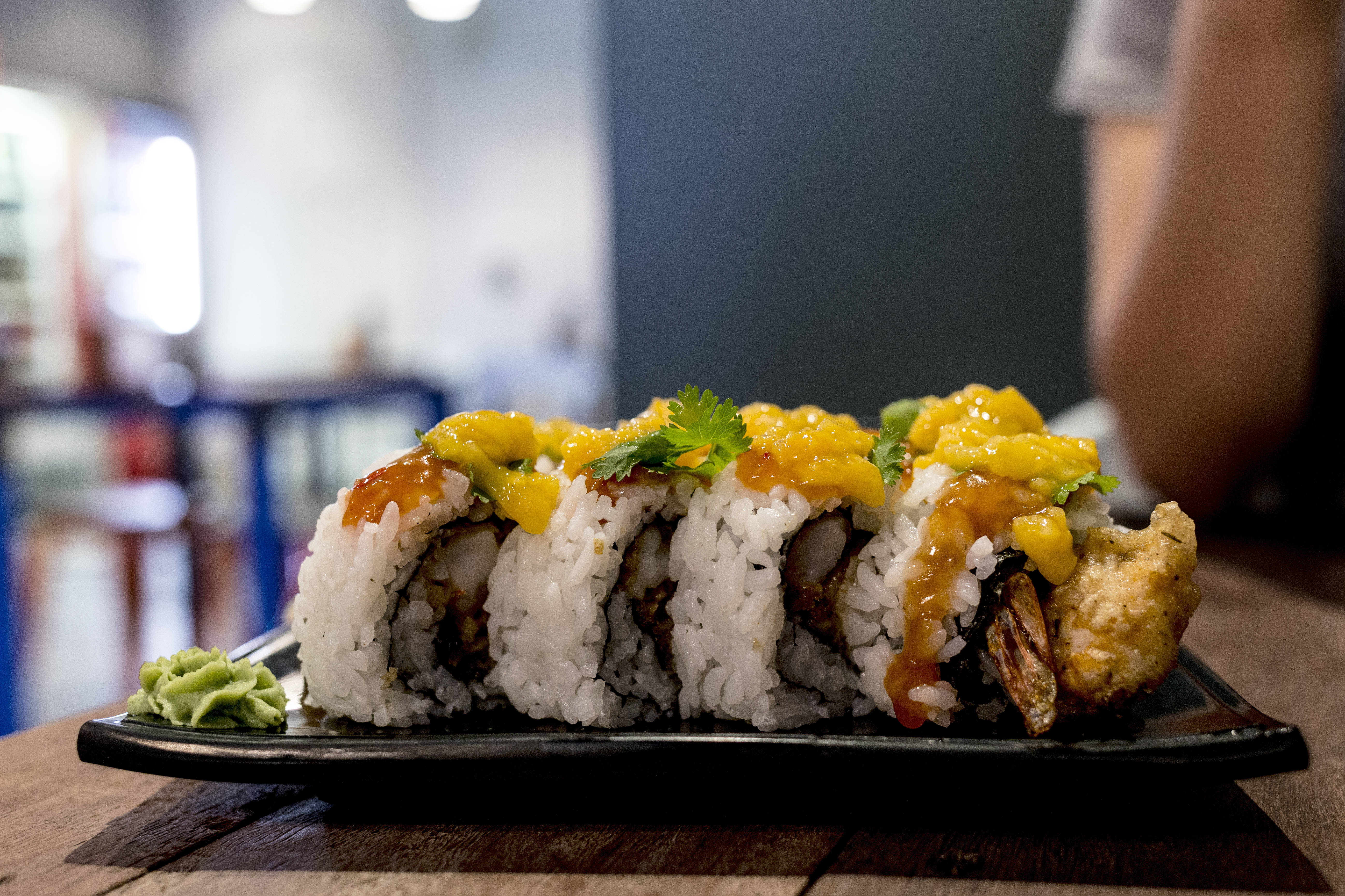 A vibrant plate of mango chicken sushi, featuring tender chicken pieces wrapped in fluffy rice, drizzled with sweet mango sauce, garnished with fresh cilantro, and served with a side of wasabi for an added kick. A delightful fusion of tropical and savory flavors