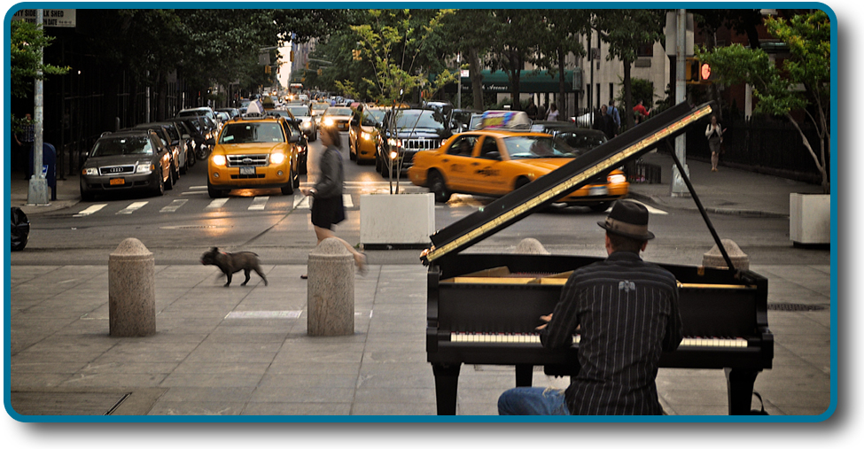 Une photographie montre une personne jouant du piano sur le trottoir près d'un carrefour très fréquenté d'une ville.