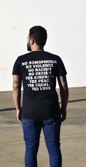 Black male with his back to the camera wearing a black t-shirt that reads: No homophobia, No violence, No racism, No sexism, Yes Kindness, Yeas peace, Yes equality, Yes love