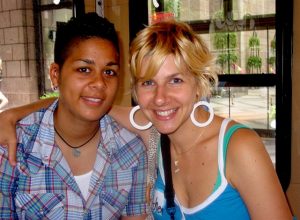 Young lesbian couple smiling at the camera, one woman has her arm around the other