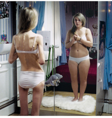 Phot of a girl with anorexia standing in front of a mirror. The image being reflected shows a female that is fat.