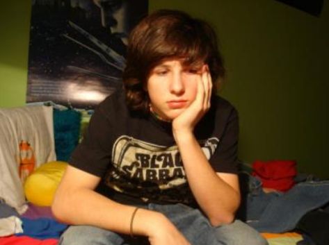 An unhappy-looking teenaged boy sitting in his bedroom.