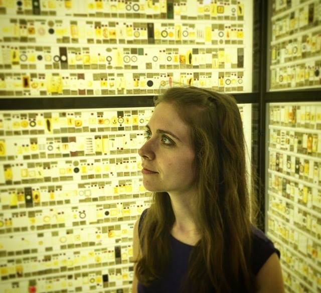 A woman with long light brown hair stands in front of screen with scientific data and imagery.