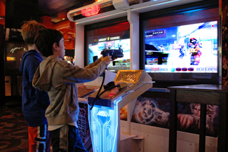 Una fotografía muestra a dos niños jugando un videojuego y apuntando un objeto similar a un arma hacia una pantalla.