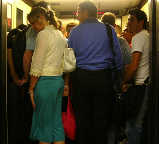 Un ascenseur bondé est montré. De nombreuses personnes se tiennent près les unes des autres.