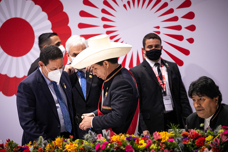 Peru's President Pedro Castillo stands with other campaign officials. President Castillo wears a large straw hat, while the other officials wear suits and ties without anything on their heads.