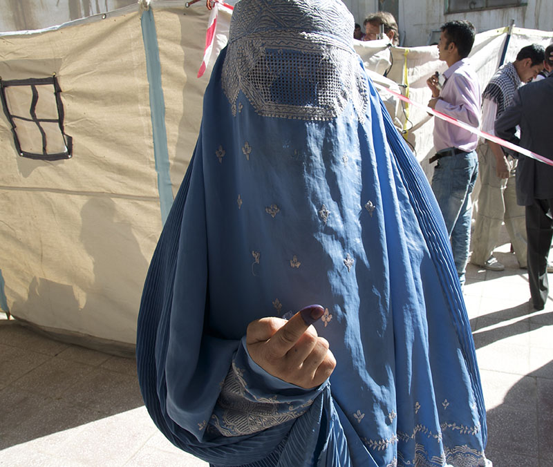 A veiled woman shows ink on her finger indicating that she has voted.