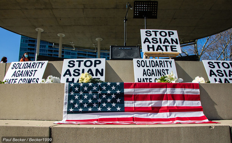 Large white signs that read “Stop Asian Hate” and “Solidarity Against Hate Crimes” are displayed above a draped American flag.