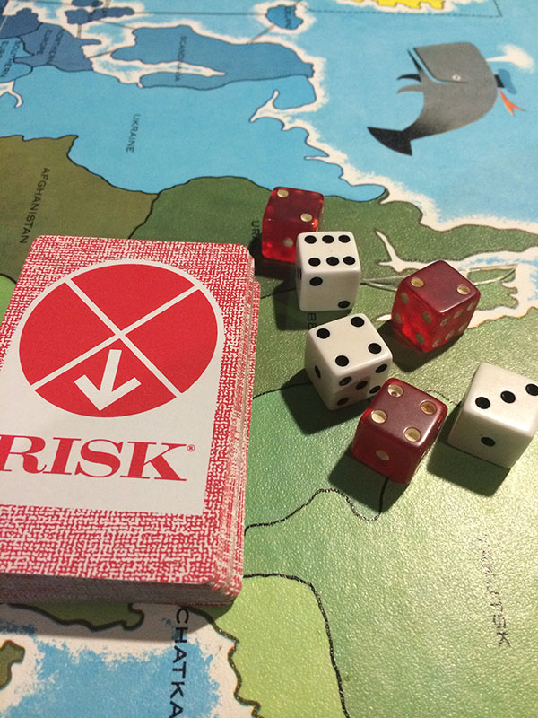 The board for the boardgame Risk is set up and in play. Three red and three white dice and a deck of game cards are placed on the board.