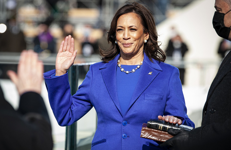 Vice President Kamala Harris raises her right hand. Her left hand rests on two books that a man holds out for her.