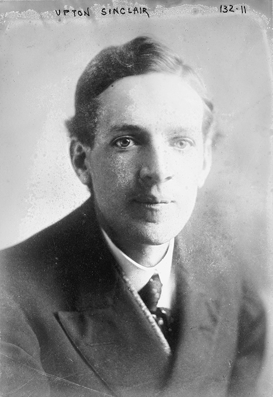 In an old black and white photograph, a person wearing a suit and tie sits for a portrait.