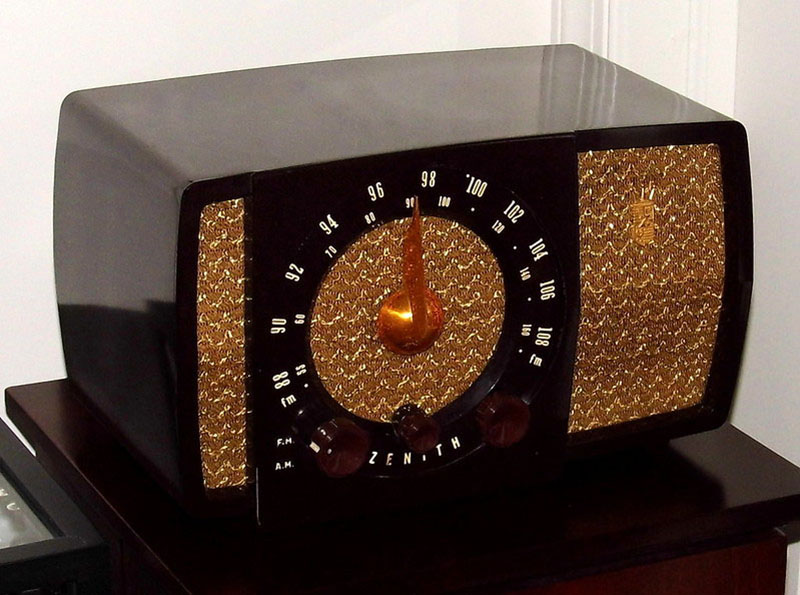A bulky, oblong radio from the early 1950s with a large dial and speakers is shown on a table top.
