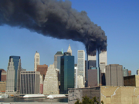 صورة فوتوغرافية تُظهر مباني مركز التجارة العالمي، بعد وقت قصير من وصول طائرتين إليها في صباح يوم 11 سبتمبر 2001. سحب كثيفة سوداء من تدفق الدخان من كلا المبنيين.