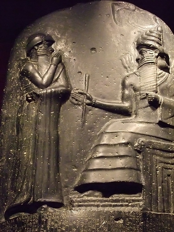 Refief scrulpture with a figure on the left standing and a figure on the right in a sitting position