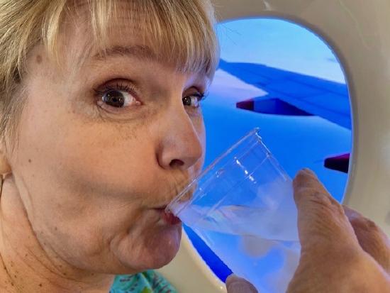 Author Cardwell sipping a drink in front of an airplane window