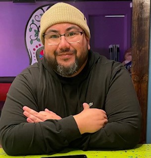Alexis in black shirt and a tan beanie smiling against a purple background
