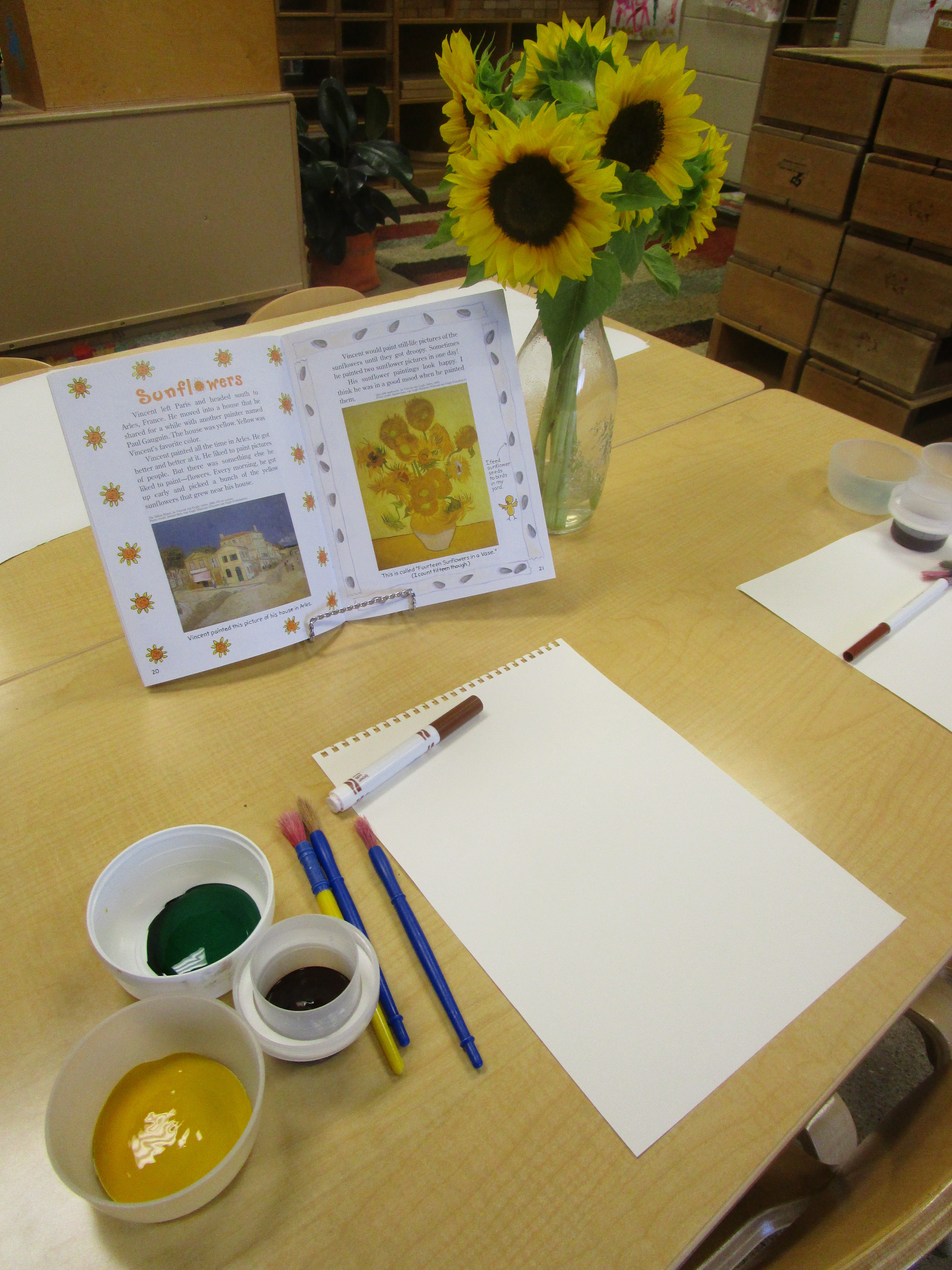 Sunflowers in vase, book on van Gogh, and watercolors with paintbrush and paper on table