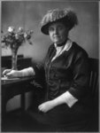 Jane Addams sits at a desk in front of a bouquet and holds a pen