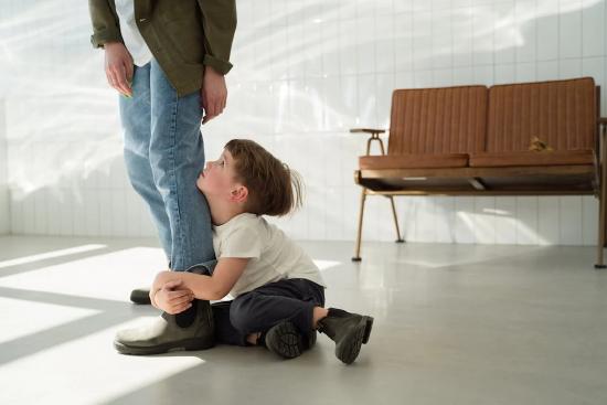 Child sitting on floor and holding on to parents leg