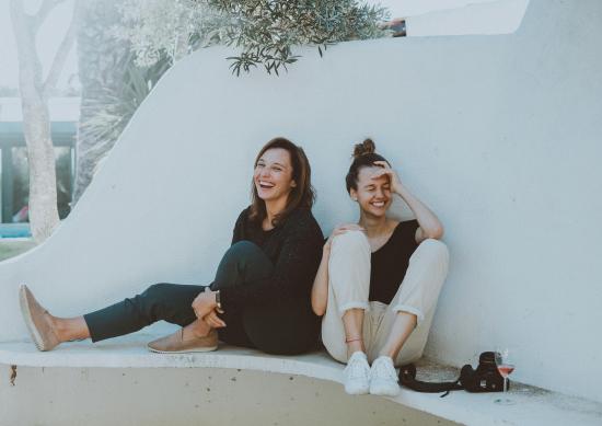 Two young women laughing and sitting on a concrete bench outdoors.