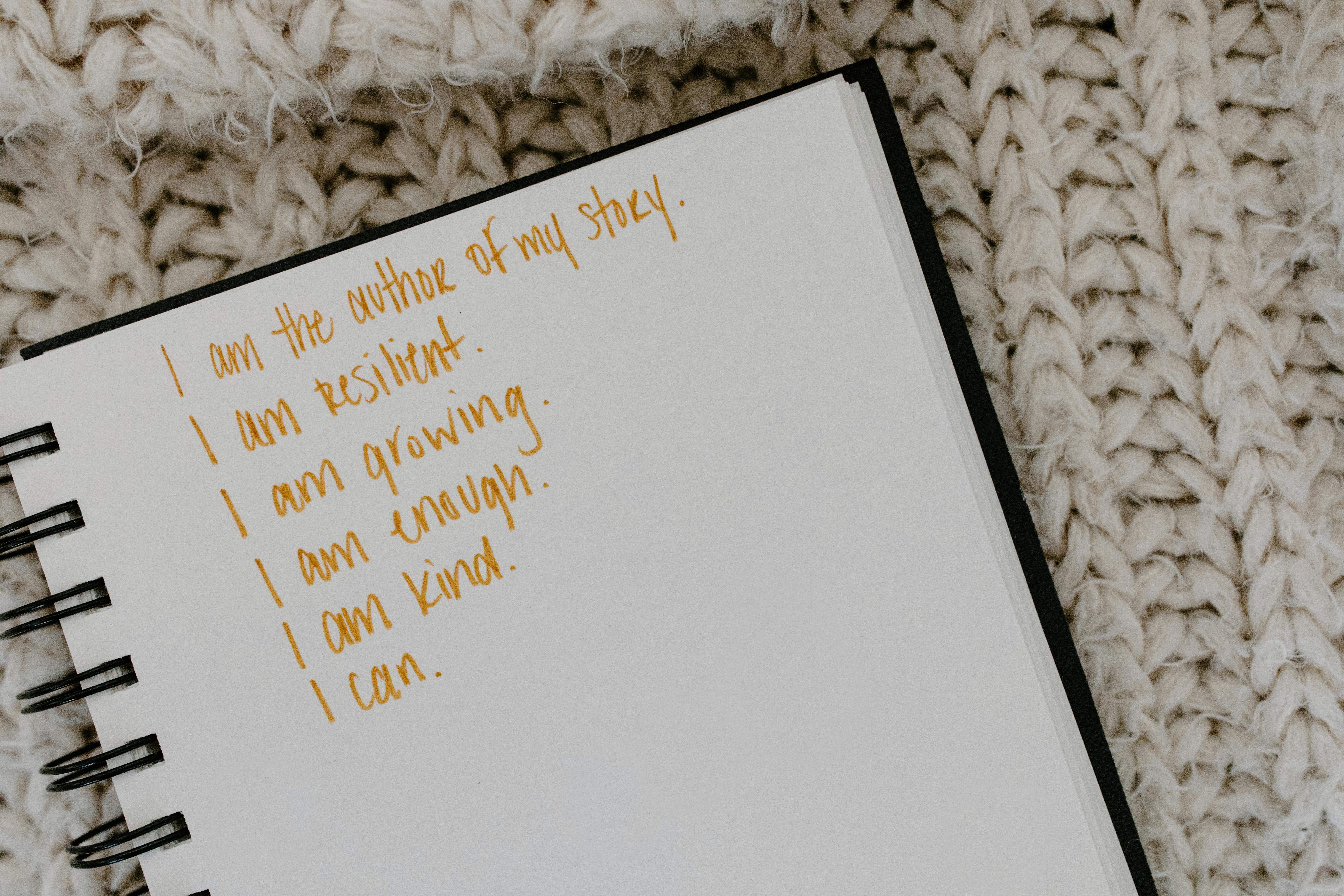 A handwritten list in orange ink on a notebook reads: "I am the author of my story. I am resilient. I am growing. I am enough. I am kind. I can."