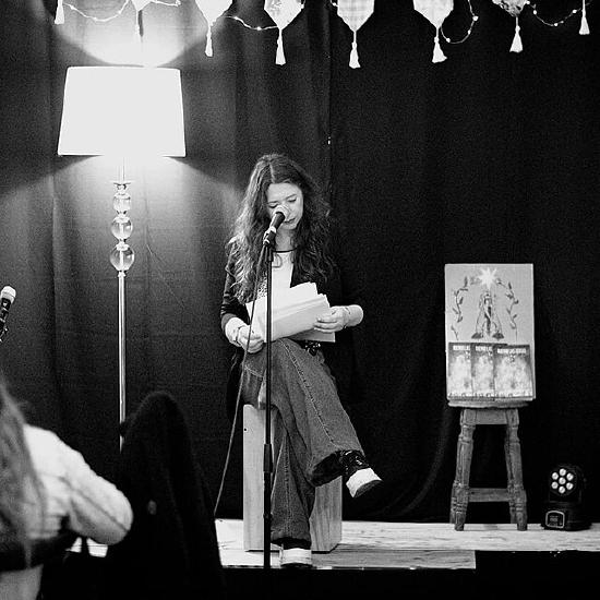 Performer sitting in a chair on stage, looking at her notes.