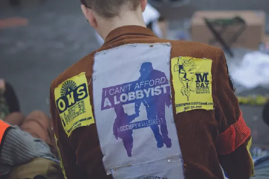 An image of the back a person wearing a jacket. A patch on the jacket reads &ldquo;I can&rsquo;t afford a lobbyist&rdquo;.