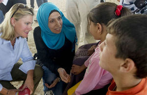 Two women in conversation with two children in a community setting, one woman wearing a blue hijab.