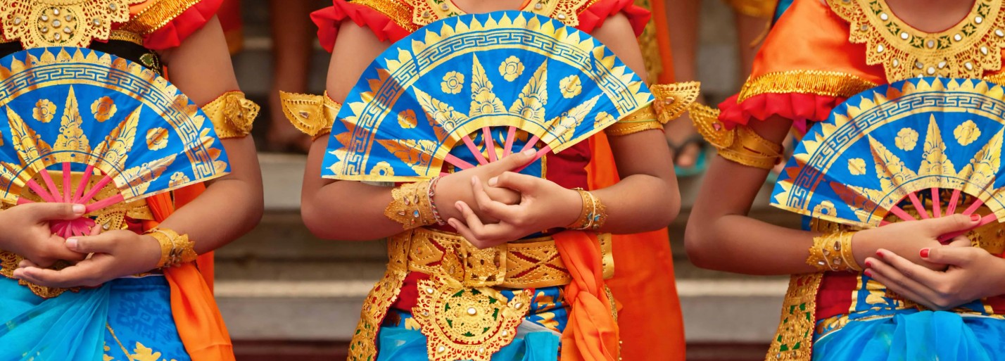 Three dancers in colorful traditional attire hold ornate blue fans