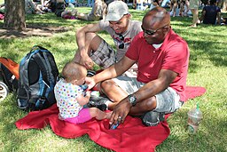 Two men sit on a blanket and play with a baby.