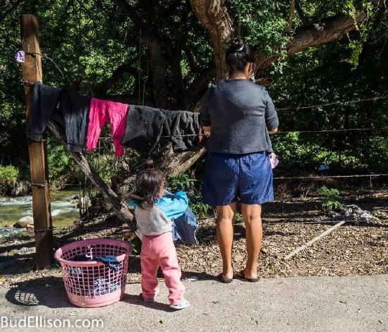 Mother hanging laundry on an outside line with young daughter "helping"