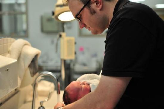 A man washing his baby's hair under a faucet.