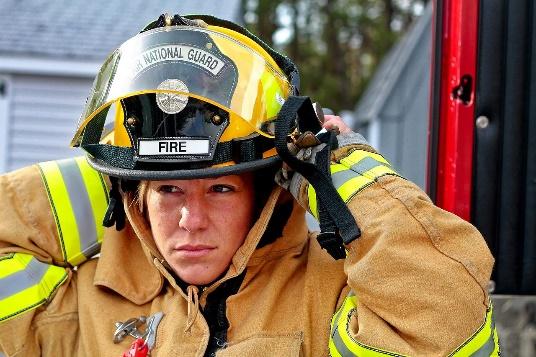 A closeup of a firefighters face as she adjusts the back of her helmet.