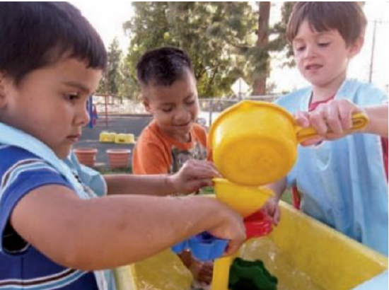 Boys playing together pouring water from a pan thru a funnel into the water trough