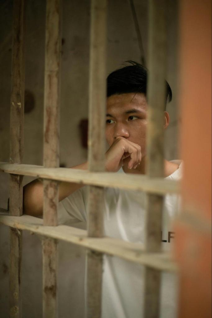 A person looking out sadly from behind the bars of a jail or prison cell.