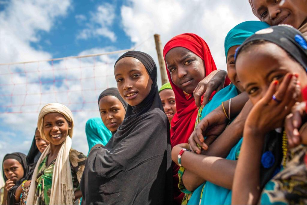 a group of dark skinned young women with head coverings look into the camera, smiling.