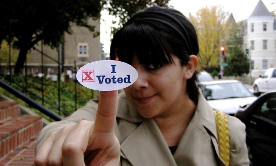 A woman with a "I Voted" sticker on her finger pointing at the camera.
