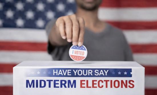 A voter drops an &ldquo;I Voted&rdquo; sticker into a ballot box, symbolizing civic participation in midterm elections&mdash;contests that, though often drawing lower turnout than presidential races, can dramatically reshape control of Congress and influence the direction of national policy.