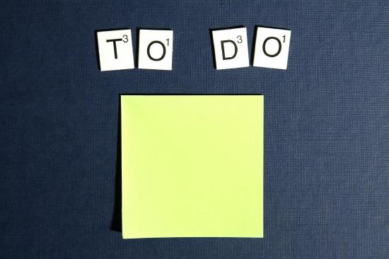A stack of post-its underneathe the words "to do" spelled out using Scrabble tiles.
