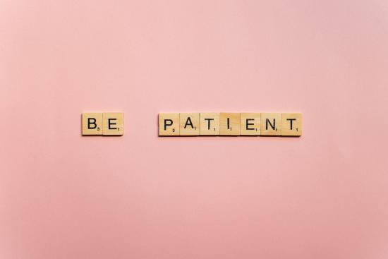 Scrabble tiles spelling out the words "be patient" on a pink background.