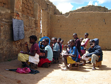 这是一张孩子们坐在被毁的建筑物中的画面，该建筑物充当他们的户外 “教室”。