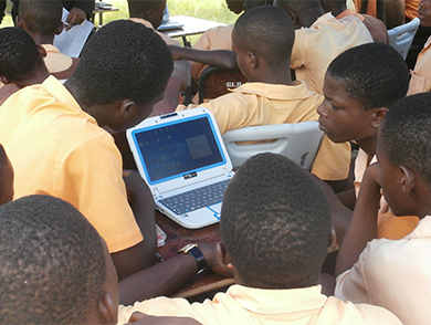 Esta fotografia mostra vários estudantes reunidos em torno de um único laptop alimentado com energia solar.