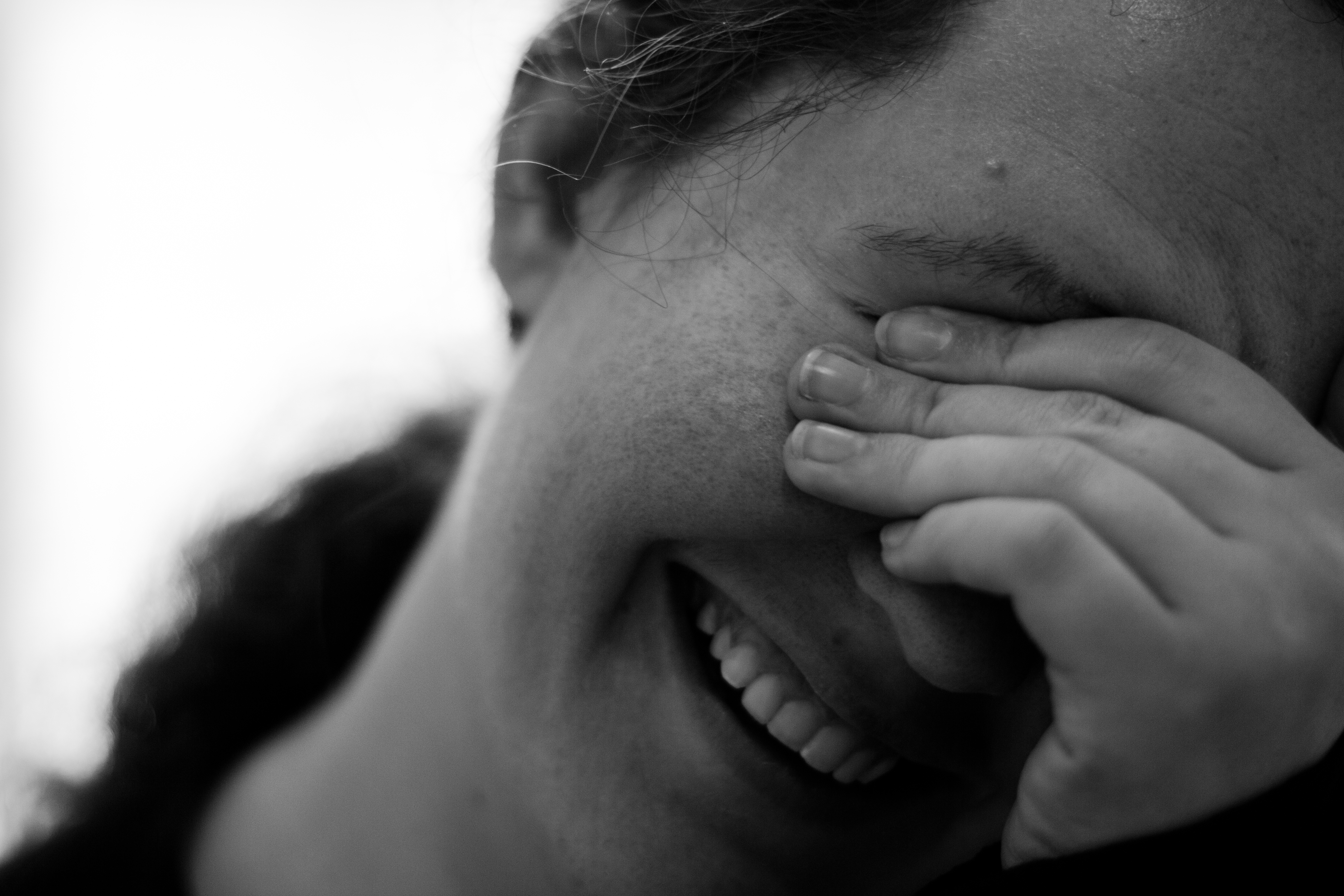 Embarrassed woman smiling and looking downward with her hand covering her eyes.