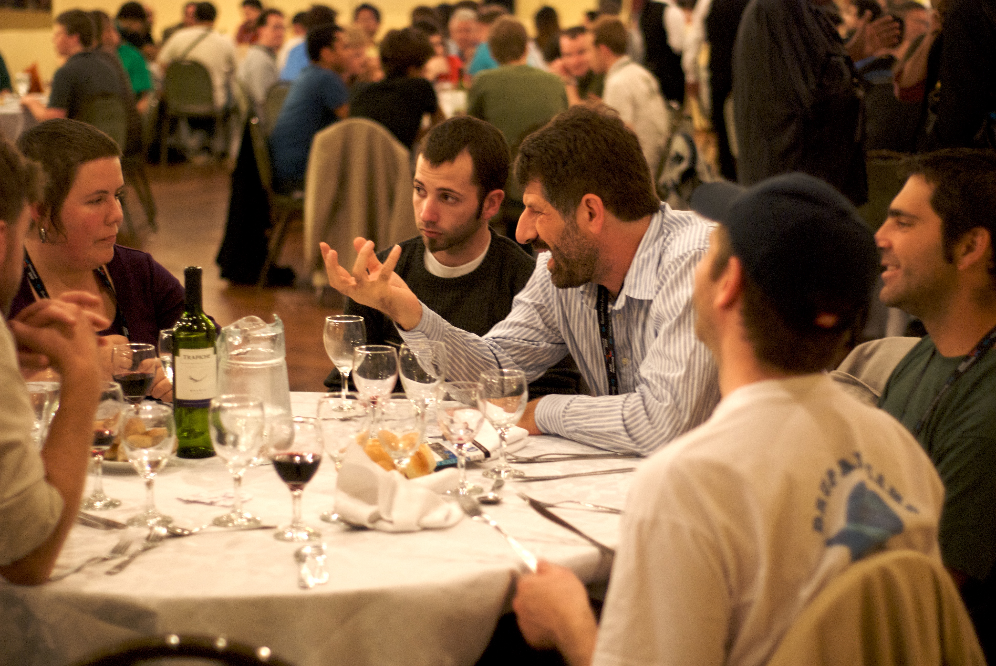 A man gestures animatedly during a conversation at a dinner table.