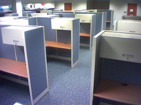 Cerca de 10 cubículos de escritório vazios são mostrados.