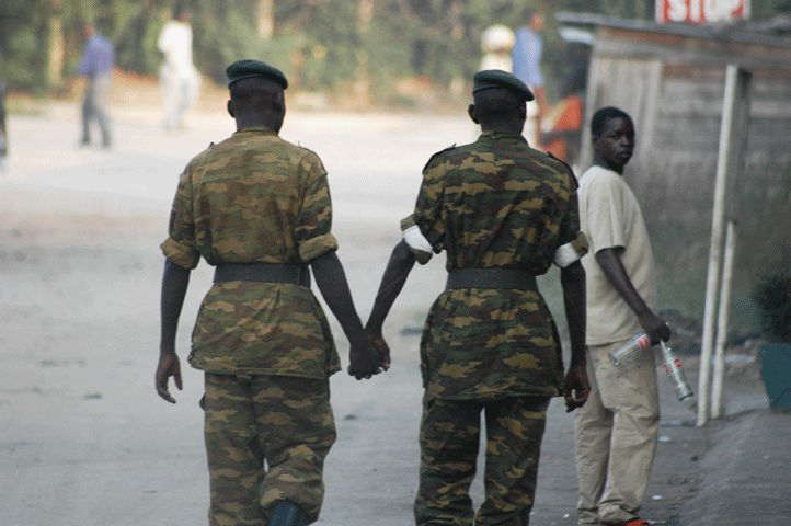 Dois soldados do sexo masculino em uniforme são mostrados por trás andando e de mãos dadas.