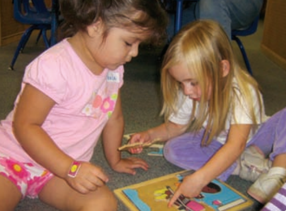 Dos niñas sentadas en el suelo y jugando con un juguete rompecabezas.