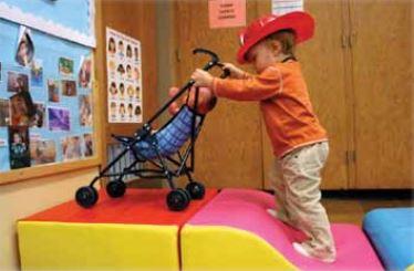 Un niño con sombrero de bombero y empujando una carriola