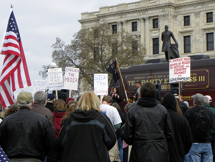 Photo d'une foule debout devant le bus Tea Party Express devant le bâtiment du Capitole de l'État pour un rassemblement