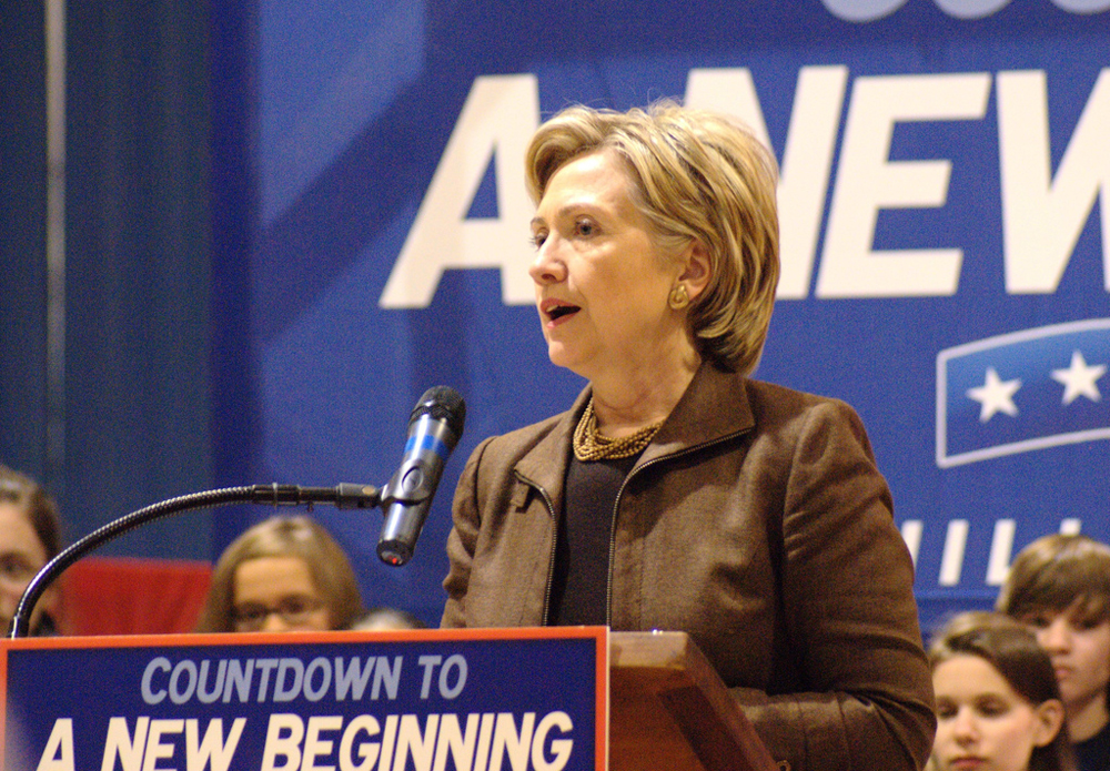 A então candidata presidencial Hillary Clinton é mostrada atrás de um pódio com um cartaz dizendo: Contagem regressiva para um novo começo. Várias crianças são mostradas em segundo plano.